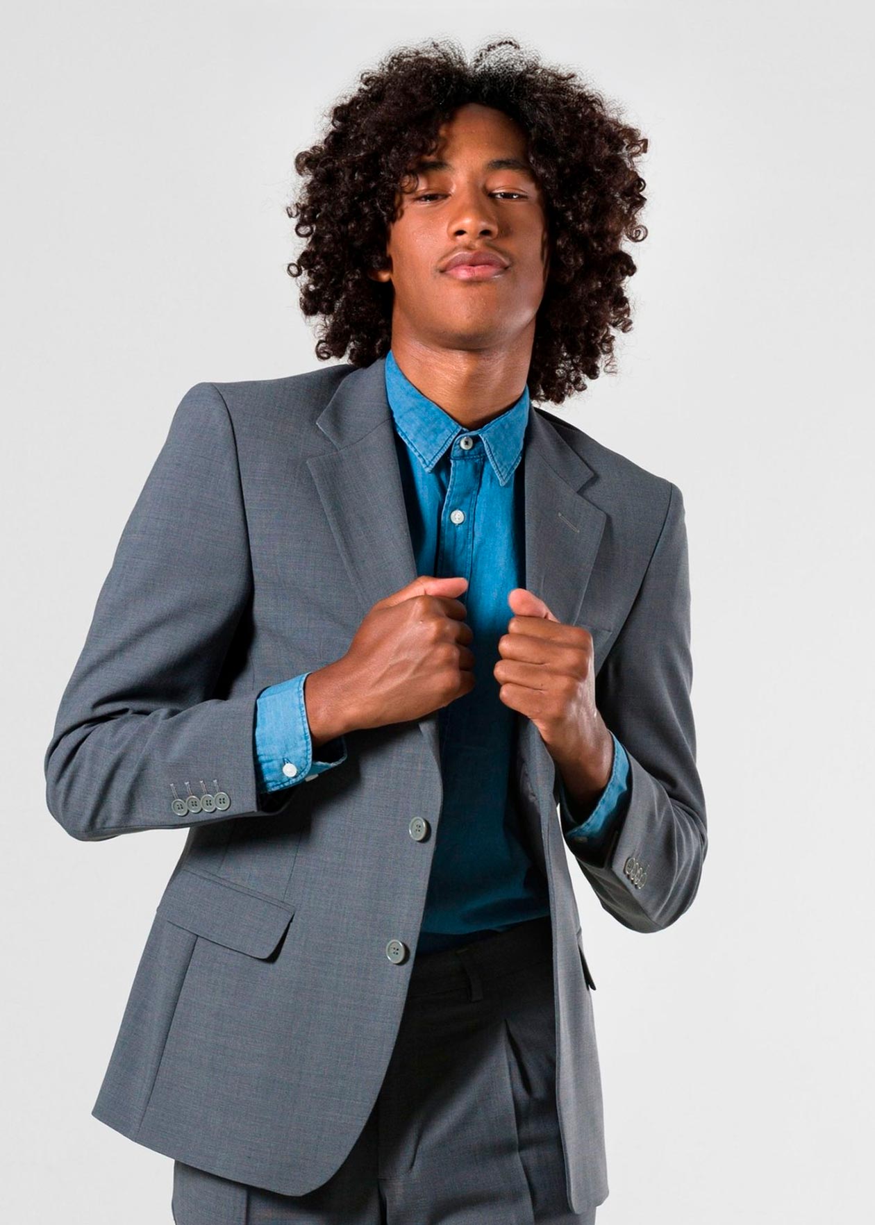 Joven con traje gris y camisa azul, posando con confianza, ideal para representar una agencia Shopify.