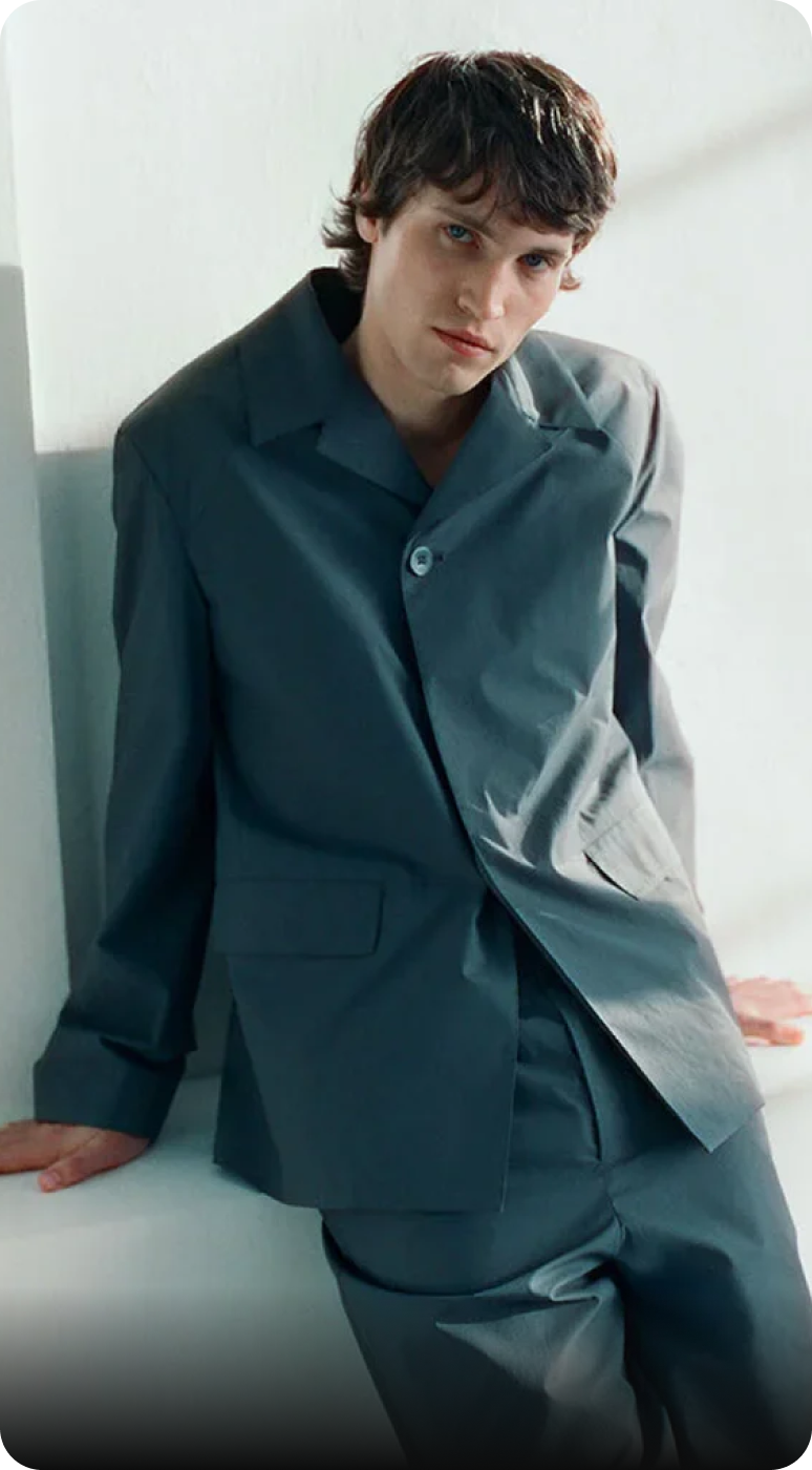 Modelo con traje gris posando en un entorno minimalista, destacando el diseño moderno y elegante.