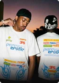 Persona con camiseta blanca con diseños gráficos en un entorno urbano al atardecer.