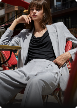 Mujer con traje gris sentada en una terraza, representando estilo y elegancia en el diseño Shopify.