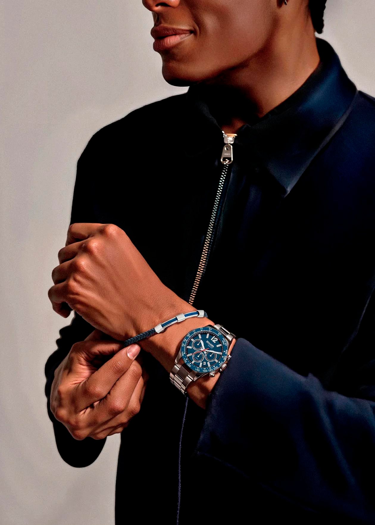 Hombre con reloj elegante en la muñeca, vistiendo una chaqueta negra con cremallera.