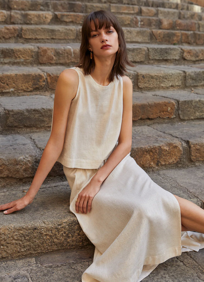 Mujer sentada en escaleras de piedra, vistiendo un vestido de lino claro, con un estilo minimalista.