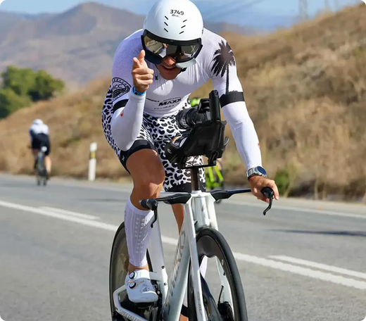 Ciclista en carretera señalando, vestido con traje deportivo y gafas, compitiendo en evento de ciclismo.