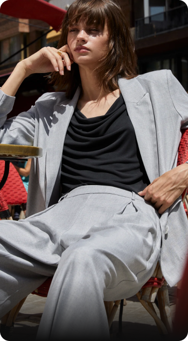 Modelo con traje gris y blusa negra, sentada en una terraza, mostrando estilo y elegancia.