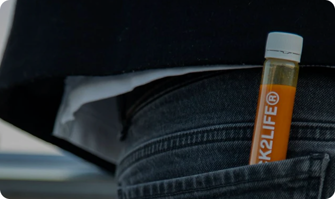 Frasco de laboratorio con líquido naranja en el bolsillo de un pantalón, fondo oscuro.