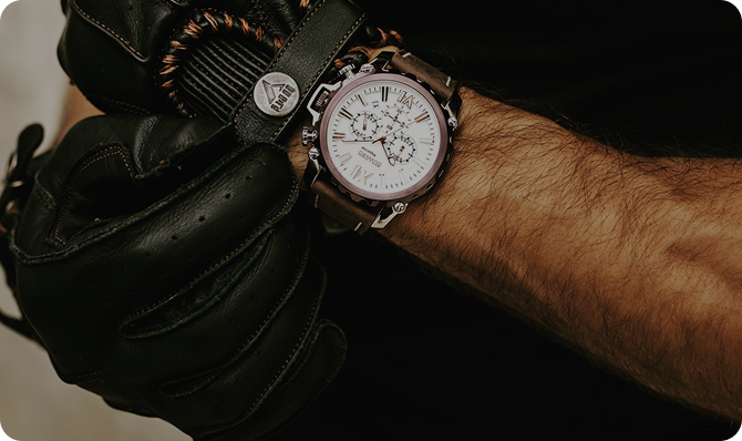 Reloj de pulsera sobre una muñeca con guantes de cuero, fondo neutro.
