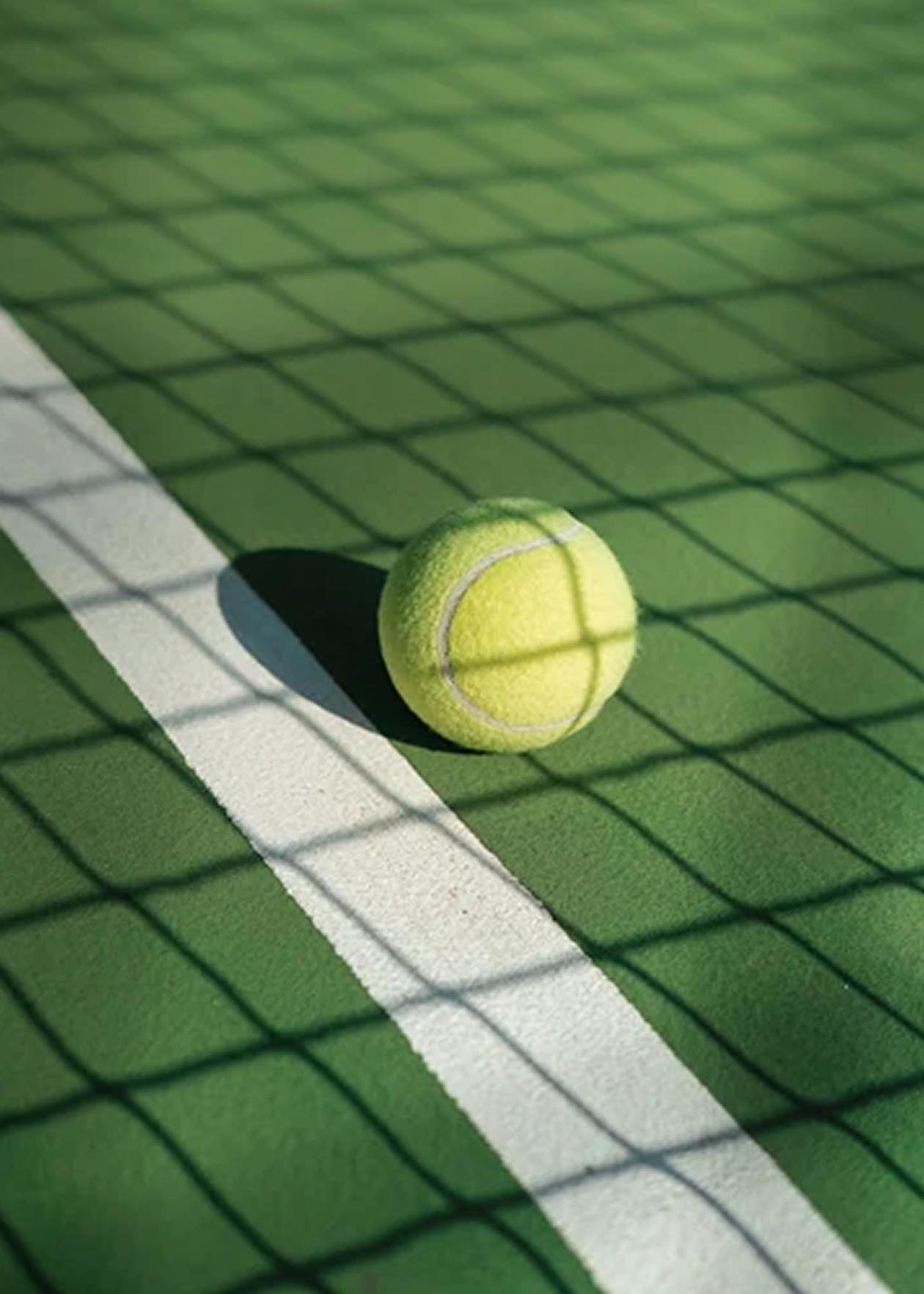 Pelota de tenis amarilla sobre una cancha verde, con líneas blancas y sombras marcadas.