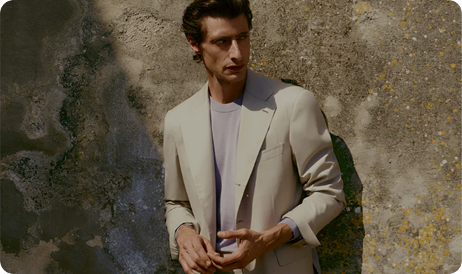 Hombre con traje claro posando frente a una pared texturizada, reflejando un estilo moderno y elegante.