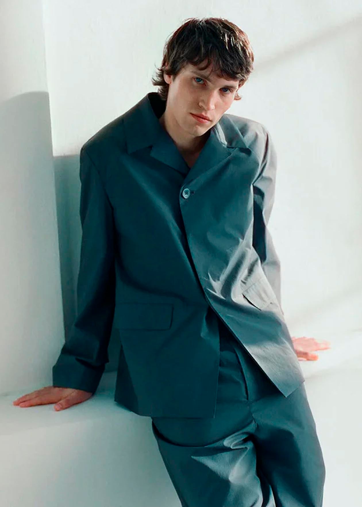 Hombre con traje azul claro posando en un entorno minimalista, con luz natural y fondo blanco.