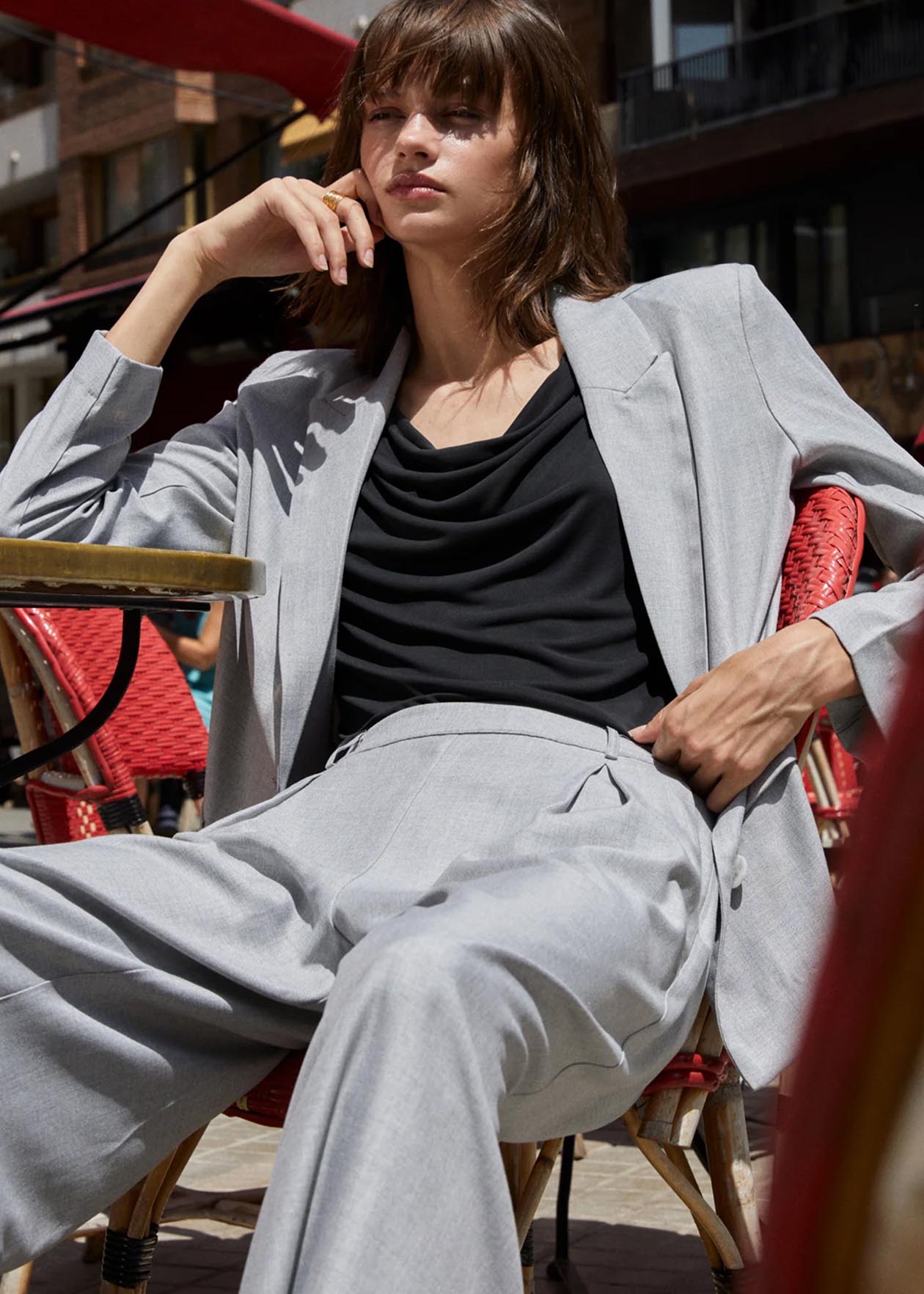Modelo con traje gris sentado en una terraza, mostrando estilo y elegancia.