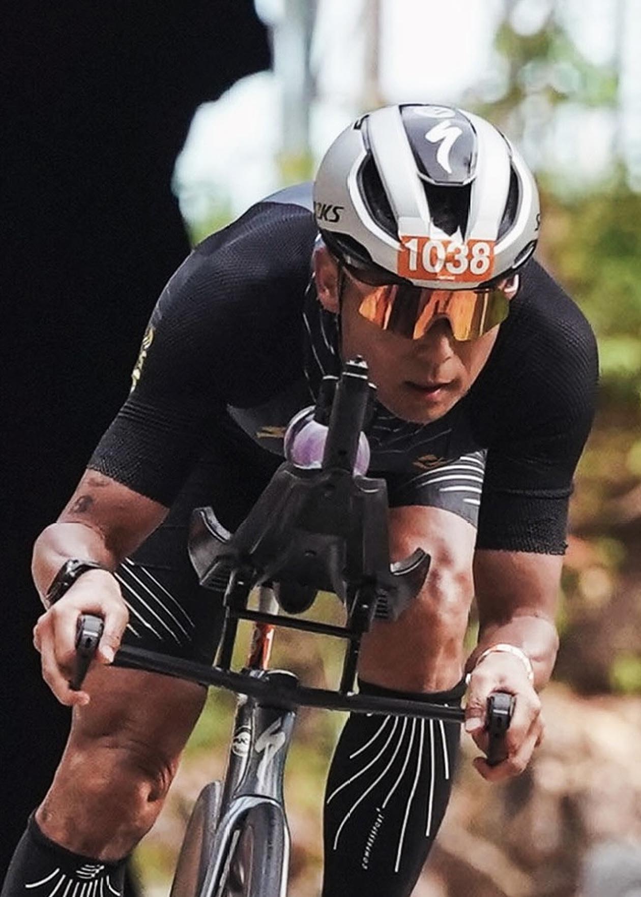 Ciclista en acción con casco y gafas, compitiendo en una carrera de velocidad.