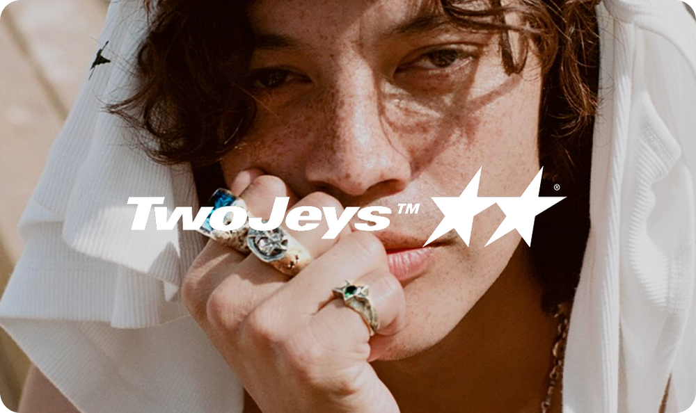 Joven con anillos en la mano y mirada pensativa, fondo desenfocado, estilo casual.