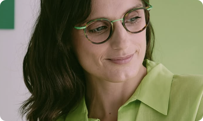 Mujer con gafas y blusa verde, sonriendo, en un entorno que evoca diseño moderno y fresco.